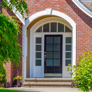 front entry door surrounded by white trim, windows and red brick house