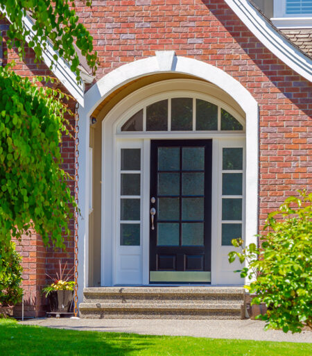 front entry door surrounded by white trim, windows and red brick house